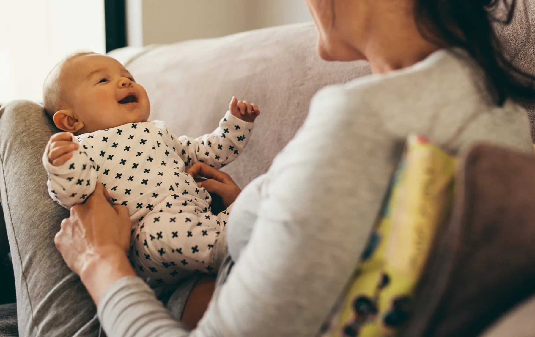 Mother smiling at her baby while holding them on a couch at home